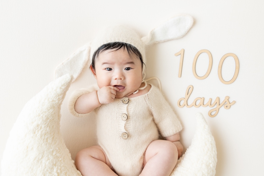 うさぎの衣装を着た生後100日の男の子の赤ちゃんが、指を咥えてカメラ目線になっている、スタジオでの撮影の様子