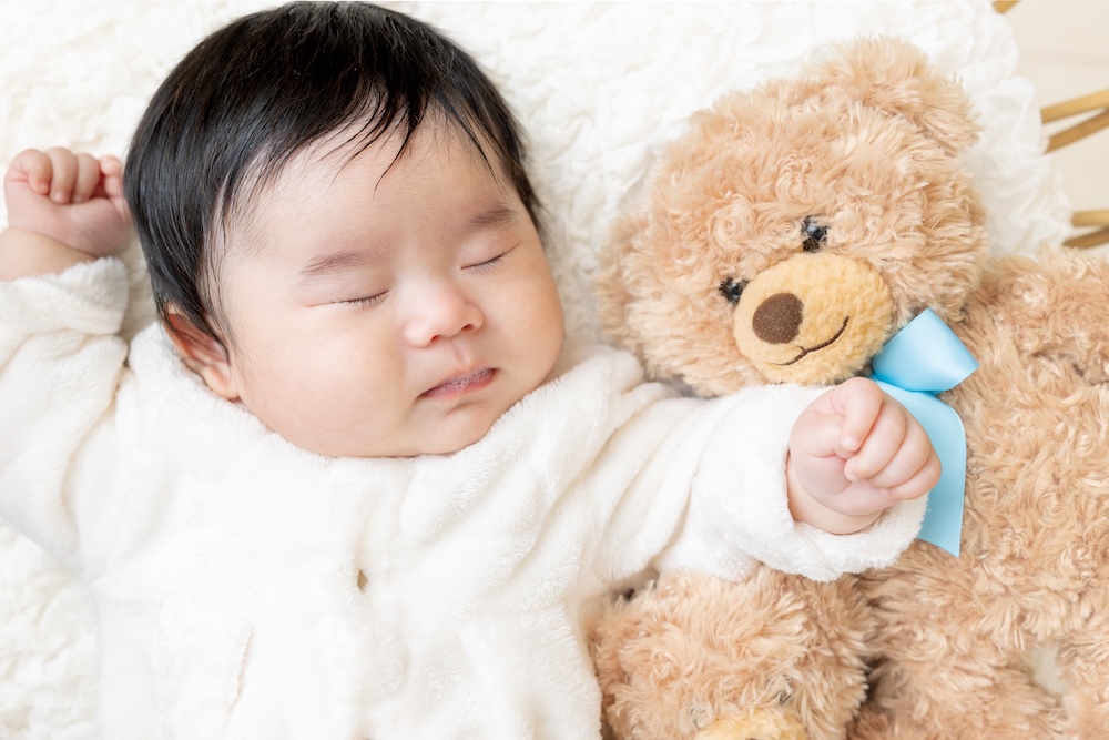 生後100日の男の子の赤ちゃんがクマのぬいぐるみと一緒にベッドに寝転がっている撮影中のオフショット