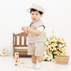 1歳の男のがスタジオでバースデー写真を撮影・ベージュのハンチング、ベスト、ズボンを着用して、不思議そうな顔で振り向いている様子