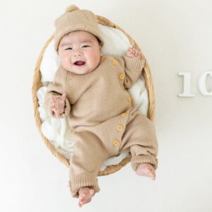 生後100日の男の子が、ベージュのニットロンパース、お揃いの帽子をかぶっている、スタジオでの衣装着用写真