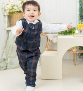3歳の男の子がチェックのベスト、ズボンのセットアップスーツを着てスタジオで楽しそうに走り出す衣装の紹介写真