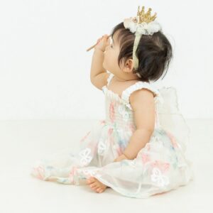 背中に蝶々モチーフがついたドレスを着ている1歳の女の子の写真