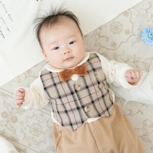 蝶ネクタイにチェックのベストを着て仰向けに寝転んでいる赤ちゃんの写真