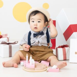 白いベレー帽をかぶって、蝶ネクタイにサスペンダーがついたズボンを履いている1歳の子どもが写っている写真