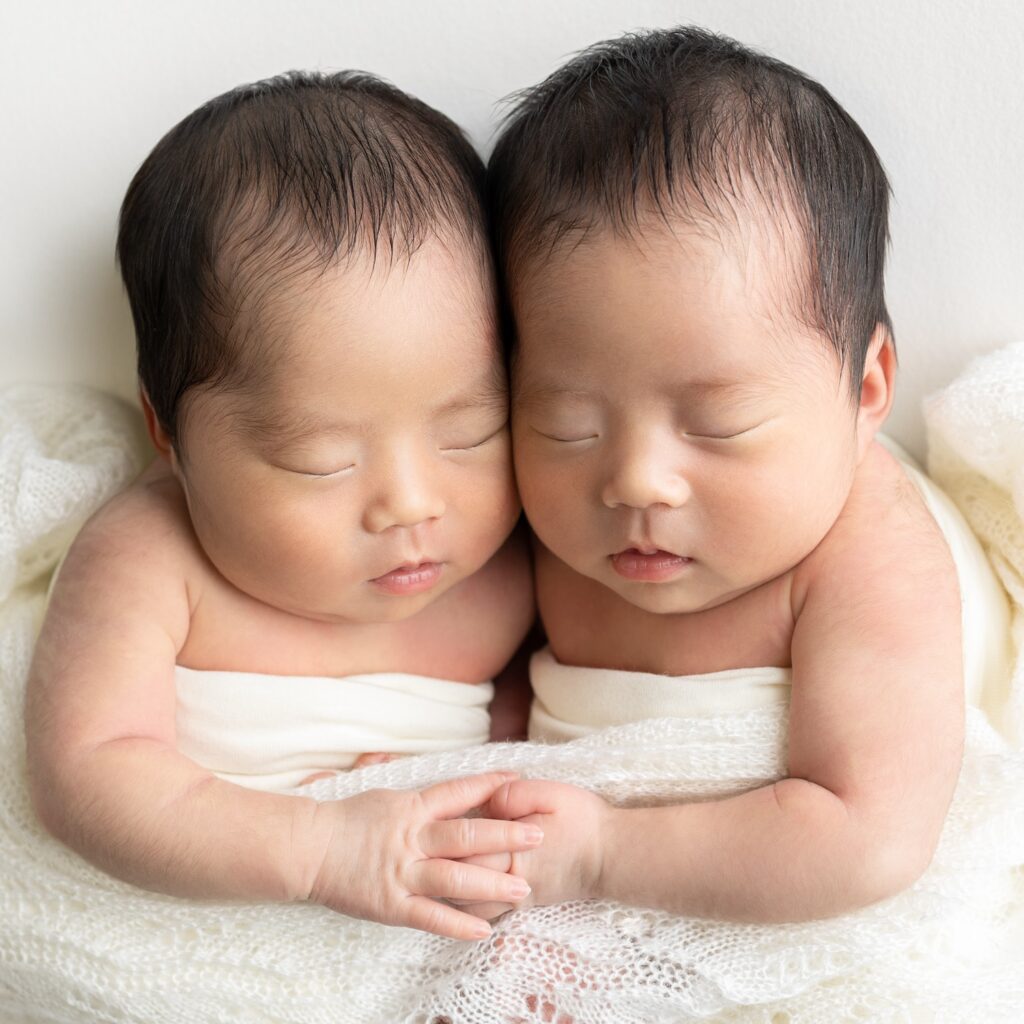 新生児の双子の姉妹が手を取り合って、ねんねしているニューボーンフォト撮影の写真