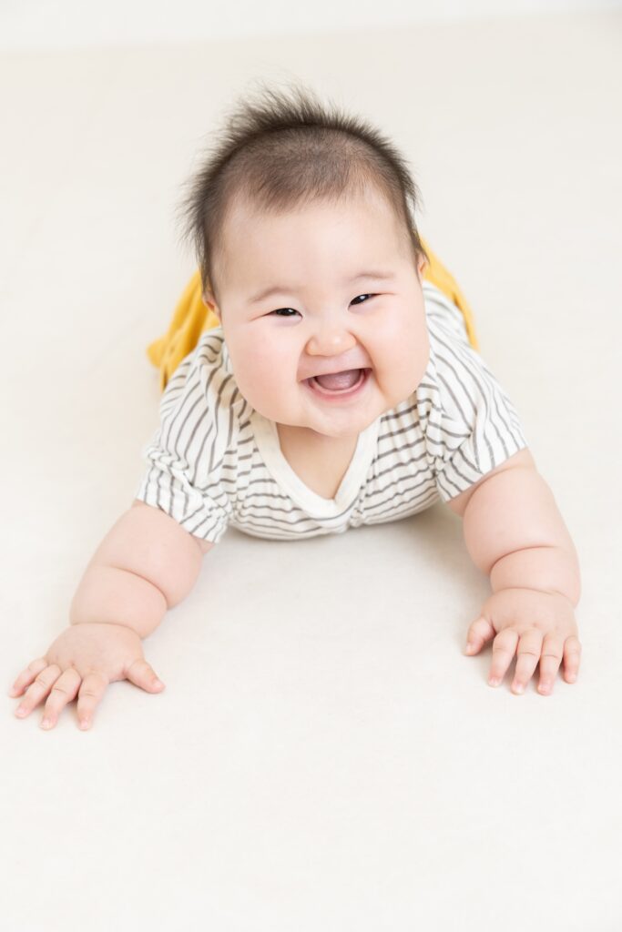 生後6ヶ月の女の子の赤ちゃんがうつ伏せになって、満面の笑みを向けてくれている、スタジオでのハーフバースデー撮影の様子