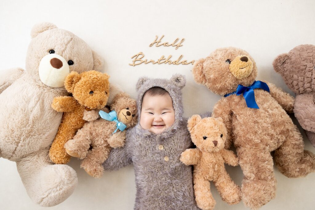 生後6ヶ月の女の子の赤ちゃんが、ふわふわ毛糸のクマさんボンネット、ロンパースを着てとびきりの笑顔を見せてくれている、ハーフバースデー撮影での写真
